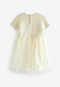 Robe en tricot de couleur crème clair avec des manches courtes, des bords festonnés et une jupe en tulle superposée ornée de broderies florales et de boutons au dos.
