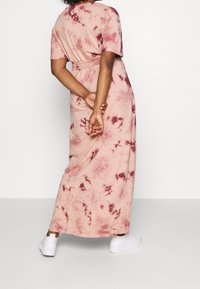 Maksimekko pehmeästä vaaleanpunaisesta kankaasta, jossa on burgundin värinen sidostekniikka, lyhyet hihat ja yhdistelevä vyö vyötäröllä, yhdistetty valkoisiin lenkkareihin.