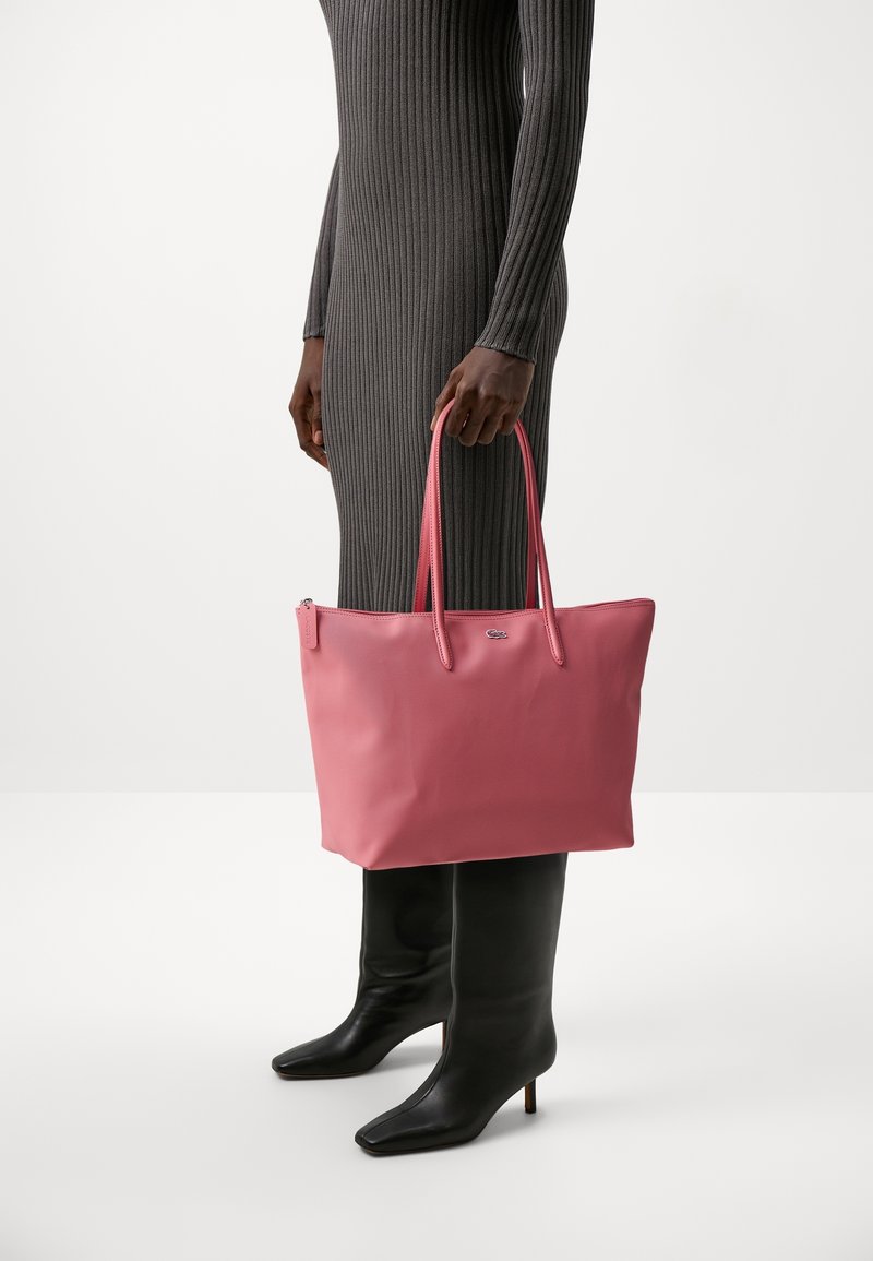 Sac fourre-tout rose avec une finition texturée et des poignées doubles, exposé aux côtés d'une robe grise côtelée ajustée et de bottes noires jusqu'aux genoux.