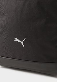 Crna tkanina ruksak s teksturiranom površinom, s bijelim skakačim Puma logotipom sa strane i glatkim crnim dnom.