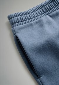 Blå sweatshirtstof med elastisk talje, der har en glat tekstur og sidesømme, vinklet til nærbillede af materiale og farve.