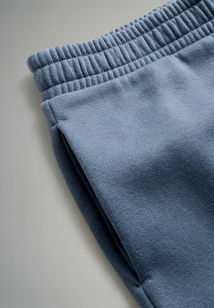 Plava majica od dukserice s elastičnom waistband, s glatkom teksturom i bočnim šavovima, nagnuta za bliski pregled materijala i boje.