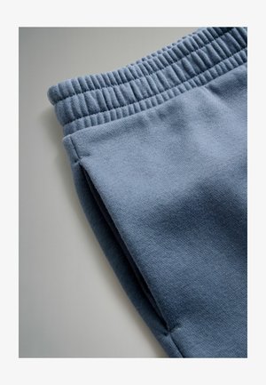 Kék pulóver anyag rugalmas derekú pánttal, sima felülettel és oldalsó varrásokkal, közelről bemutatva az anyag textúráját és színét.