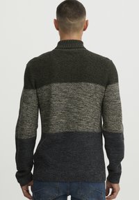 Strikkegenser med høy krage, med stripete mønster i mørkegrønn, grå og marineblå. Teksturert stoff med ribbestrikket mansjetter, faller til hoftene.