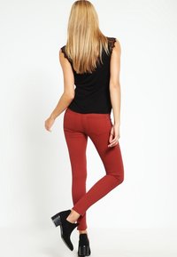 Czerwone jeansy slim fit w połączeniu z czarnym topem bez rękawów z koronkowymi akcentami. Stylizacja obejmuje czarne botki za kostkę i eksponuje dopasowaną sylwetkę.