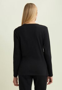Maglietta nera a maniche lunghe con scollatura rotonda e una trama liscia e morbida. Vista posteriore, design attillato che si estende fino ai fianchi.