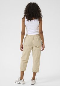 Pantalon beige rayé à taille élastique, coupe fuselée et courte, tissu texturé, porté avec un débardeur blanc et des baskets de couleur claire.