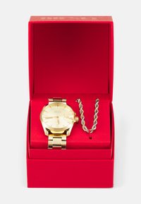 Goldfarbene Edelstahl-Uhr mit rundem Zifferblatt und Gliederband, präsentiert in einer roten Box mit goldenem Innenraum und einer silbernen gedrehten Kette.