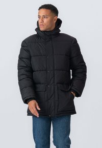 Sort pufferjakke med høj krave, frontknapper og to sidelommer. Har et quiltet design og hætte.