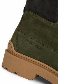 Zielone zamszowe botki z czarnymi akcentami, wyposażone w gumową podeszwę i wytłoczone logo "TOMMY JEANS" z boku. Niskoprofilowy design, teksturowane wykończenie.