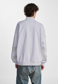 Ljusgrå sweatshirt med hög krage, lös passform och kontrasterande ränder på ärmarna. Ribbad nederkant och manschetter.