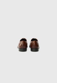 Chaussures en cuir marron avec une texture lisse, bout rond et semelle en caoutchouc noir. Présentent des coutures minimales et un design épuré.