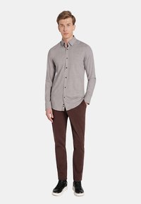 Szara koszula z guzikami, z teksturowanym wzorem, w połączeniu z brązowymi spodniami slim fit i czarnymi trampkami. Koszula posiada kołnierzyk oraz czarne guziki.