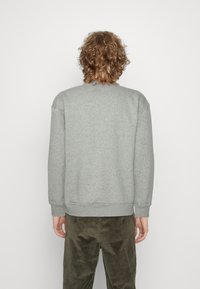 Felpa grigia realizzata in misto cotone, con colletto tondo, polsini e vita a costine. Vista da dietro, con un design semplice.