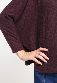 Burgundowy, luźny sweter z długimi rękawami i teksturowanym materiałem. Charakterystyczny design z obniżoną linią ramion oraz swobodny krój.