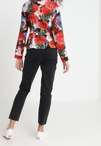 Haut peplum floral noir avec des fleurs colorées rouges et violettes ; associé à un jean noir fuselé et des baskets blanches, vu de dos.