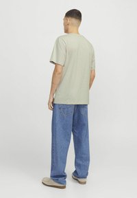 Hellgraues Baumwoll-T-Shirt mit kurzen Ärmeln, kombiniert mit lockeren blauen Jeans. Das Outfit hat eine entspannte Passform und betont Komfort und Einfachheit.