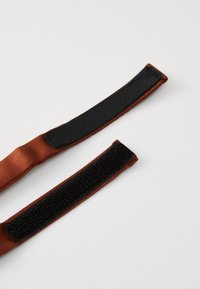 Sangles en tissu brun avec des sections en Velcro noir à une extrémité. Texture lisse avec un léger éclat, conception robuste et flexible.