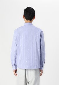 Blue striped button-up shirt with white paint splatter, long sleeves, and a collar, made of lightweight fabric, featuring buttoned cuffs.