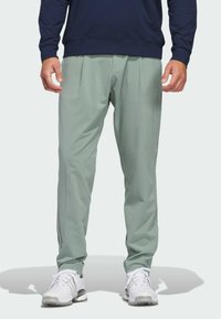 Light green athletic pants with a textured pattern, featuring a loose fit and tapered legs, paired with white athletic shoes.