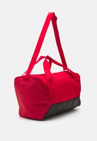 Rød duffel bag med sort bund, med rektangulær form, dobbelt bærehåndtag og justerbar skulderrem. Tekstureret stof.