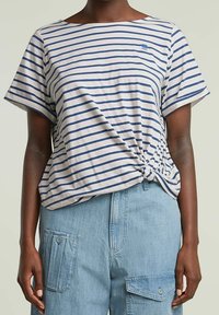 Top de manga corta a rayas en crema claro con rayas horizontales en azul marino; cuenta con un detalle de nudo en el costado y un ajuste relajado.