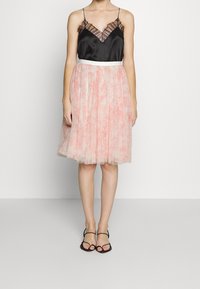 Un camisol en satin noir avec des dentelles et une jupe en tulle plissé rose, avec une ceinture blanche. Des sandales noires à fines lanières complètent le look.
