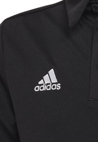 Czarny t-shirt polo wykonany z gładkiego materiału, z nadrukowanym na srebrno logo Adidas na lewej piersi oraz zapinaną na guziki kolnierzykiem.