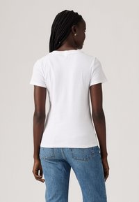 Valkoinen lyhythihainen t-paita, joka on valmistettu puuvillasta, jossa on pyöreä pääntie, slim fit -malli ja sileä pinta. Yhdistetty vaalean sinisiin farkkuihin.