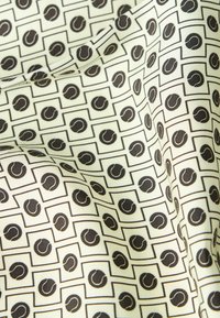 Kreemitaustaline kangas, millel korduv muster mustadest tennisepallidest, mis asuvad mustade äärtega ruutudes, nähtavate voltide ja tekstuuriga.