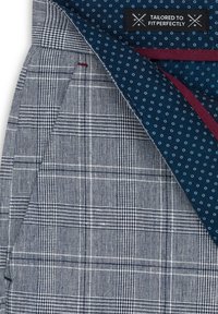 Szary materiał w kratę o strukturalnym splocie, z niebieską podszewką w kropki i czarną metką z napisem "SKROJONY, ABY IDEALNIE PASOWAĆ".