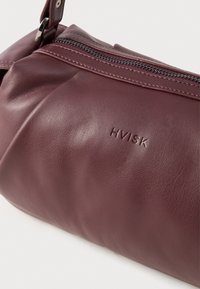 Sac à main en cuir bordeaux avec une texture lisse, doté d'une fermeture éclair et du logo de la marque en relief "HVISK". Design de pli subtil et accents en métal.