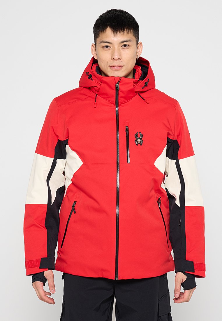Rote Jacke mit weißen und schwarzen Akzenten, hohem Kragen, Reißverschluss und mehreren Reißverschlusstaschen. Hergestellt aus wetterfestem Material.