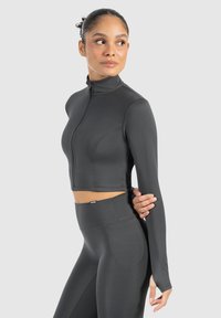 Mørkegrå cropped atletisk jakke med høj krave og lange ærmer, lavet af glat, strækbart materiale, parret med matchende leggings.