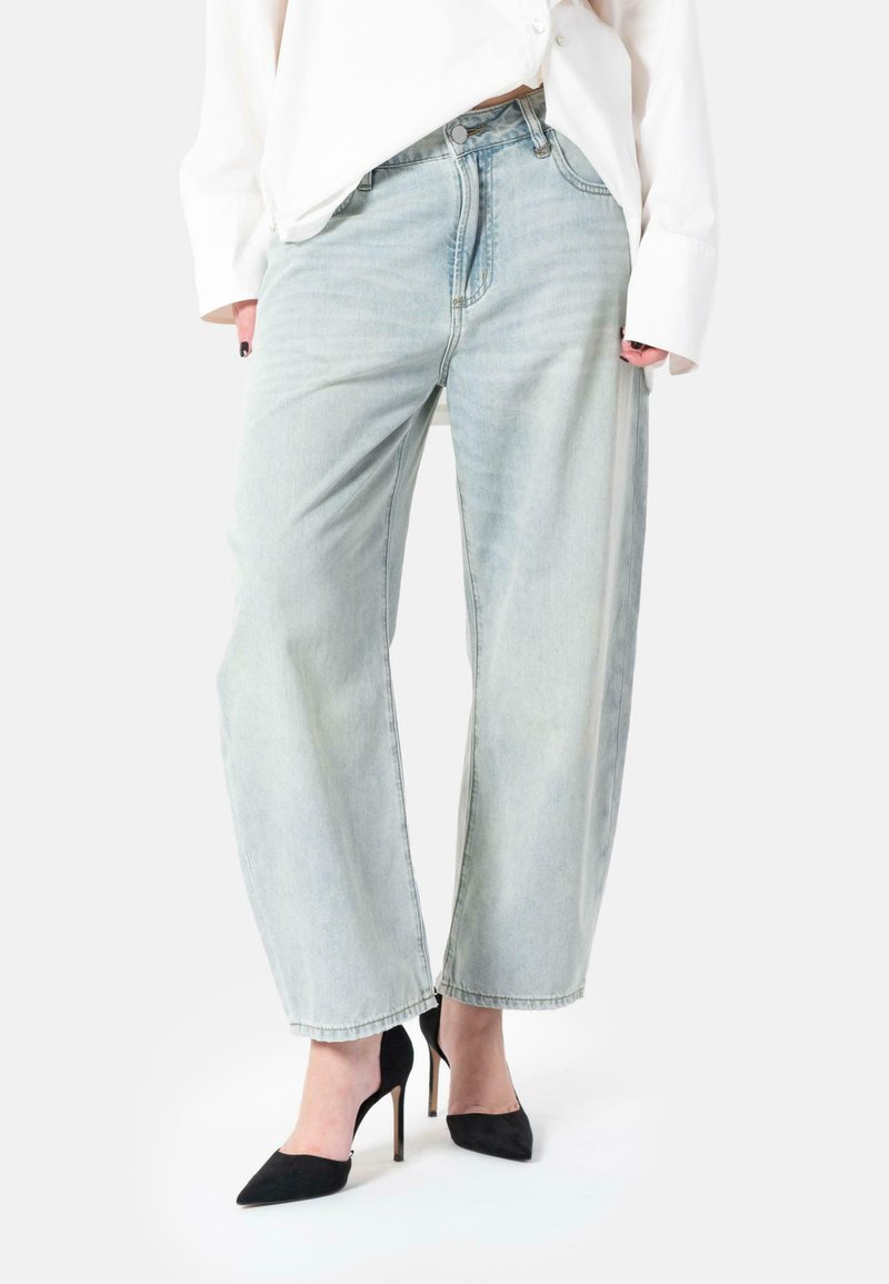 Lyseblå vidbukser laget av denim, med høy midje, falmet tekstur og subtil sømdetalj, kombinert med svarte høye hæler.