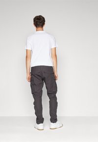 Tmavě šedé cargo kalhoty s několika postranními kapsami, doplněné bílým krátkým tričkem a bílými teniskami.