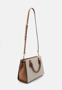Borsa rettangolare color tan e beige con stampa monogram di MK, manici corti e tracolla lunga regolabile, mostrata in diagonale su sfondo bianco.
