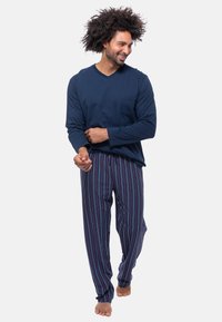 Top a maniche lunghe blu navy con scollo a V e tasca sul petto abbinato a pantaloni del pigiama a righe blu, rossi e bianchi. Tessuto morbido, vestibilità comoda.