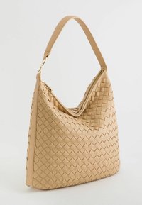 Beige vævet håndtaske med en afslappet design, en enkelt bærehank og lynlåslukning, prydet med et tekstureret mønster og glatte kanter.