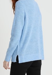 Maglione lavorato a maglia azzurro chiaro con maniche lunghe, bordi a coste e spacco laterale, caratterizzato da un motivo testurizzato su tutta la superficie.