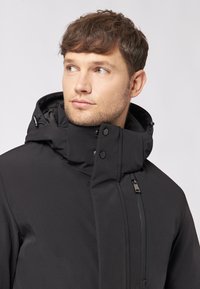 Czarna ocieplana kurtka z wysokim kołnierzem, wyposażona w napy i zamek błyskawiczny. Gładka faktura i minimalistyczny design z funkcjonalnymi detalami.