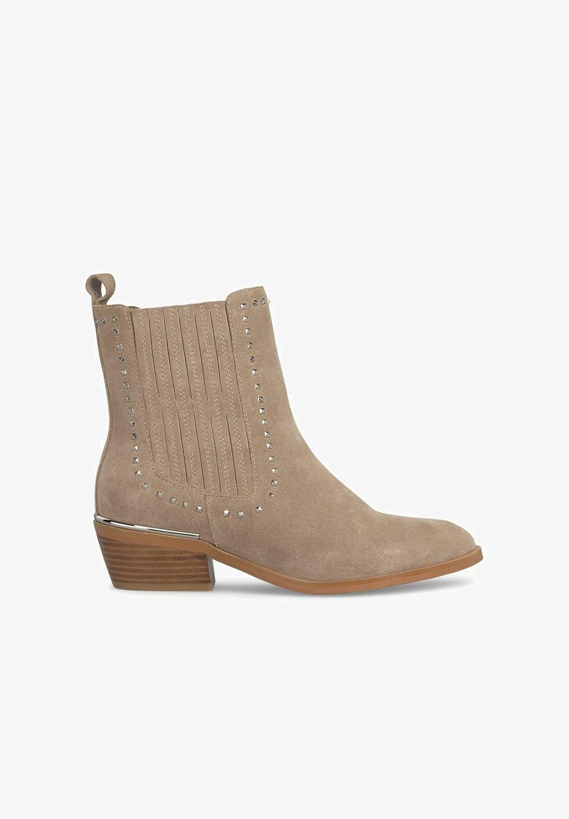 Beżowy zamszowy botek za kostkę z wydłużonym noskiem, żeberkowym wykończeniem i srebrnymi ćwiekami wzdłuż krawędzi. Posiada niski, warstwowy obcas.