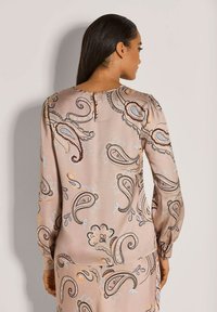 Langärmlige rosa Bluse mit Paisleymuster, die ein Schlüsselloch-Rückendetail aufweist, aus weichem Stoff besteht und mit gerafften Ärmeln für zusätzlichen Textur versehen ist.