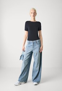 Haut à manches courtes marine, jeans larges bleu clair, baskets blanches et petit sac à main bleu clair. Matériaux lisses avec un design décontracté.