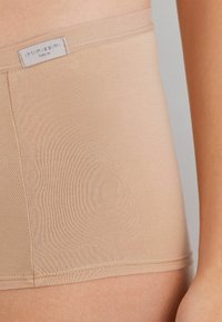 Braga de talle alto en color beige con una textura suave, ajustada y una cinturilla plana que presenta la etiqueta "Intimissimi".