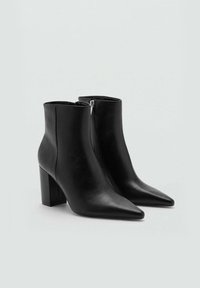 Botas de tobillo de cuero negro con puntera afilada, tacón bloque de altura media y cremallera lateral. Textura suave con un diseño minimalista.