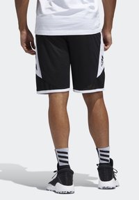 Schwarze Sportshorts mit weißen Akzenten, Netzpaneelen und einem Adidas-Logo. Getragen mit schwarzen Schuhen und grauen Socken mit Streifen.