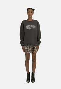 Un sweat gris avec un graphique « REALITÉS INVISIBLES », associé à une jupe à imprimé léopard et des bottines noires avec des accents argentés.