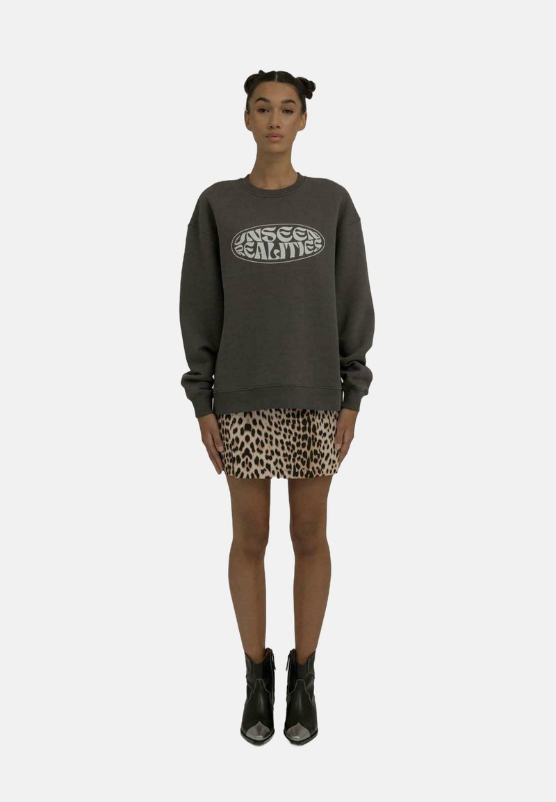 Un sweat gris avec un graphique « REALITÉS INVISIBLES », associé à une jupe à imprimé léopard et des bottines noires avec des accents argentés.