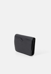 Svart lær lommebok med teksturert overflate, fold-over klaff og et V-formet aksent på fronten. Kompakt design med minimalt med maskinvare.